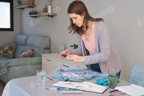 Preview: Caucasian woman taking a photo of her art design in a denim jacket.