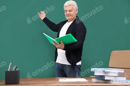 Preview: Portrait of senior teacher with notebook at green chalkboard and table
