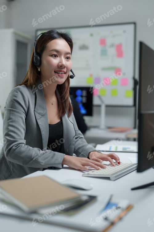 Preview: Asian businesswoman wearing headset is working and typing on keyboard in office