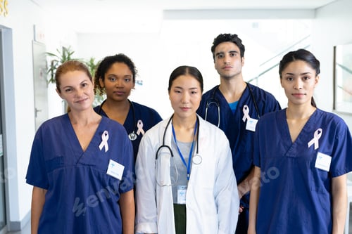Preview: Portrait of diverse group of healthcare workers wearing cancer ribbons standing in hospital corridor
