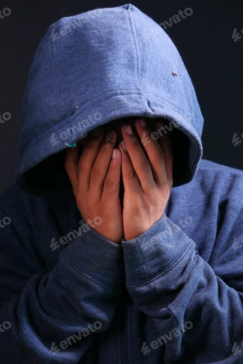 Preview: sad man in hood cover face with hands isolated in black.