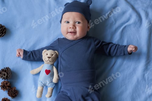 Preview: baby boy 3 months lies and smiles and holds a small toy bear in his hands.