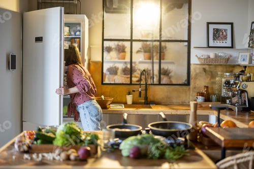 Preview: Woman looks into a fridge while cooking in the kitchen at home