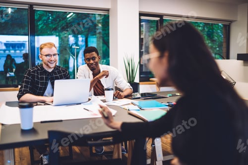 Preview: cheerful diverse business freelancers brainstorming near table desktop in workspace