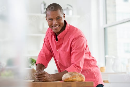 Preview: A young man in a pink shirt using a digital tablet. A loaf of bread on the kitchen counter.