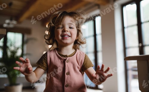 Preview: Happy small girl jumping at home, looking at camera