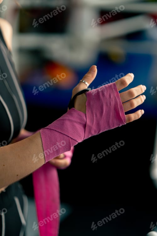 Preview: close up at a boxing fight club young girl in a black sweatshirt wraps pink elastic bandages for