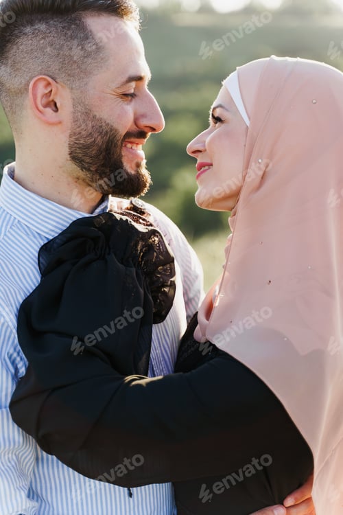 Preview: Muslim couple hugs on green hills, hijab woman smiles at her man, dating promo.