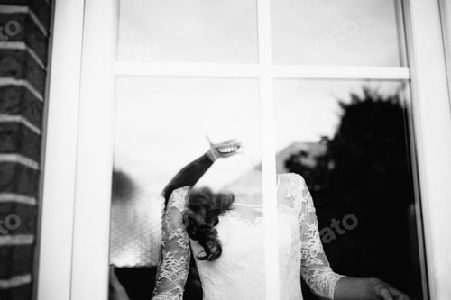Preview: he bride waits for her groom. looks happy at the window. view through the window from the street.