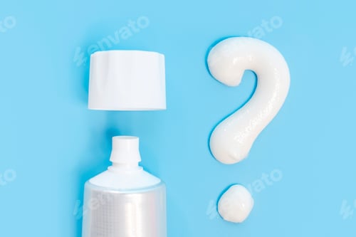 Preview: Toothpaste and question mark on blue background close-up, top view.