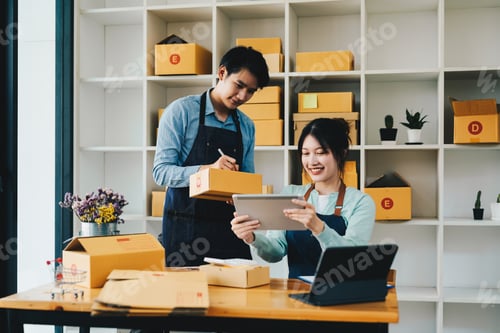 Preview: Asian couple doing online business together at home. Helping to pack products into cardboard boxes