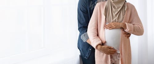 Preview: Cropped image of muslim couple expecting baby hugging near window at home