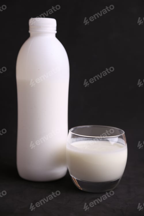 Preview: Vertical shot of a white plastic bottle and a transparent cup full of milk
