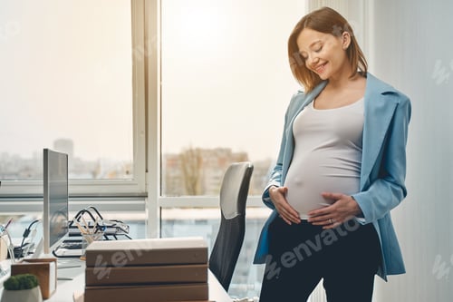 Preview: Joyful pregnant woman standing in modern office