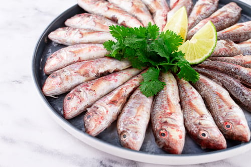 Preview: Fresh mullet fish, laid out on a large platter, garnished with lime slices and cilantro, top view,