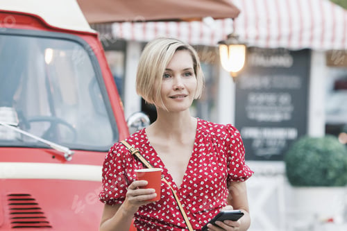 Preview: Beautiful woman drinking coffee on the go and talking on the phone on the street