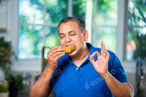 Preview: Indian asian mid age handsome man eating chicken leg piece with happiness