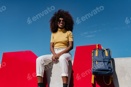 Preview: Black woman with curly hair sitting on a wall