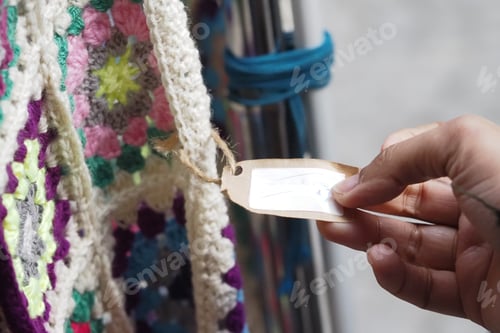 Preview: Hand reaching for a tag on a colorful crochet blanket