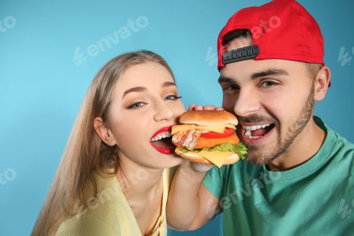Preview: Happy couple eating burger on color background