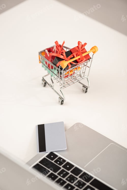 Preview: Laptop with credit card and toy gifts in cart on table