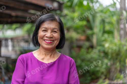 Preview: Smiling Asian elderly woman look at camera standing posing outside at home