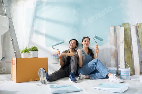 Preview: Portrait Asian couple repairing and painting the wall with blue paint using a roller renovation