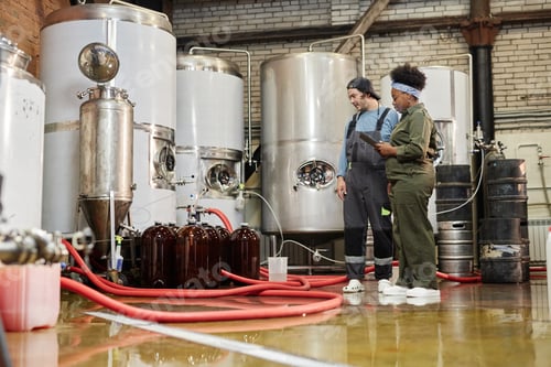 Preview: Male Production Operator and Female Technician Inspecting Tanks with Cider indoors