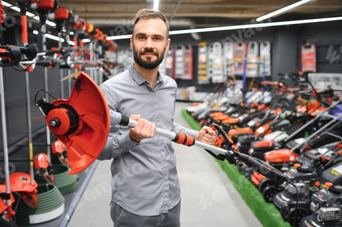 Preview: a young man in a gardening equipment store chooses an electric trimmer for mowing lawn grass