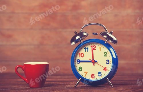 Preview: Cup of coffee and alarm clock on wooden table.
