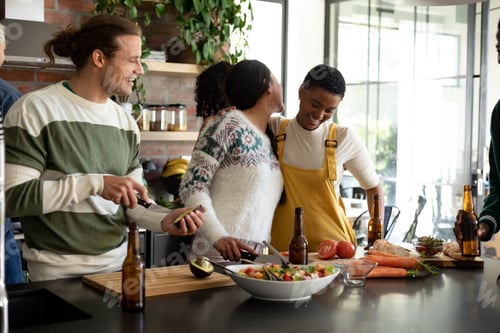 Preview: Group of happy diverse female and male friends drinking beer and cooking together in kitchen