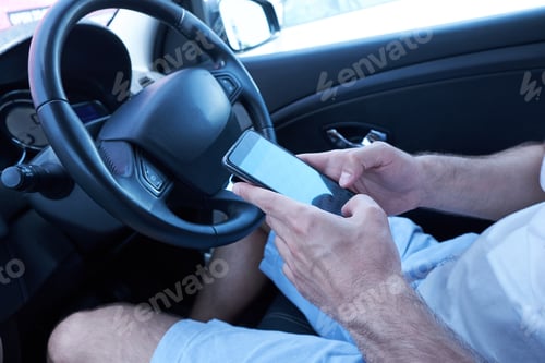 Preview: Asian man sitting in car with mobile phone in hand texting while driving