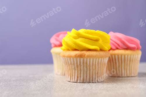 Preview: Delicious cupcakes with bright cream on gray table against violet background, space for text