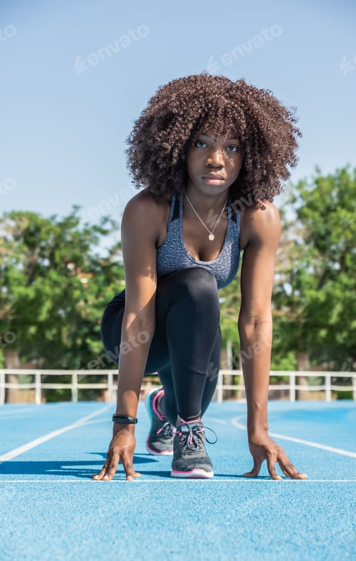 Preview: young black athlete girl with afro hair crouching down ready to start a race