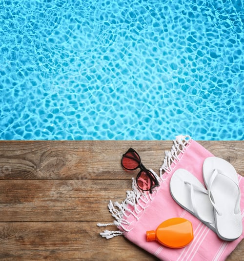 Preview: Beach accessories on wooden deck near swimming pool, flat lay. Space for text