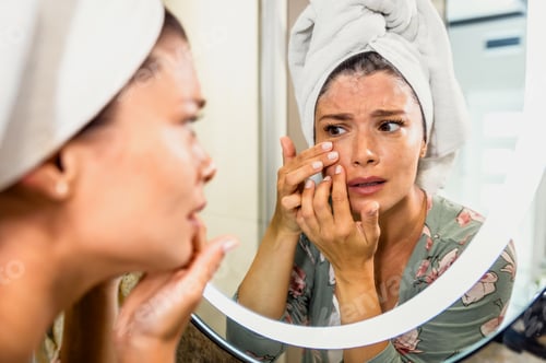 Preview: Worried woman looking in bathroom mirror worried about wrinkles and aging.