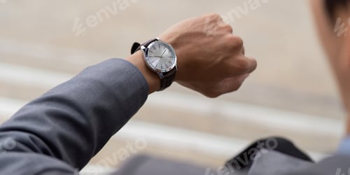 Preview: Close up of a young Asian businessman checking his watch in a modern outdoor business environment.