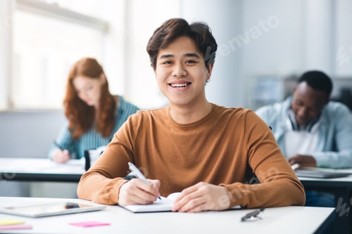 Preview: Asian male student sitting at desk writing in classroom
