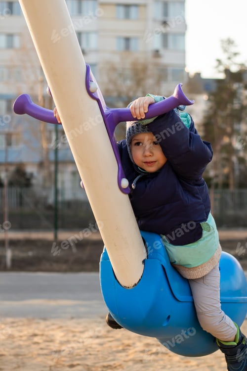 Preview: A little child rides on a colorful swing in a city park at sunset
