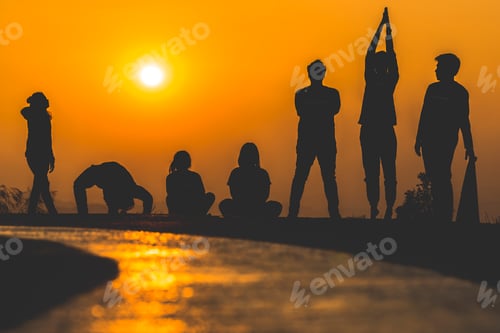 Preview: silhouette of people group practicing yoga on the beach at sunset
