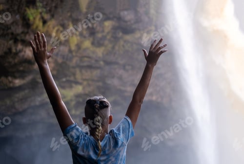 Preview: Teenage boy hands up and looking at the waterfall cascades before him.