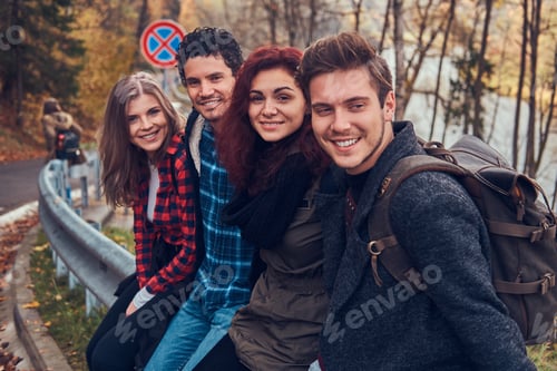 Preview: Group of young friends with backpacks sitting next to a road in forest