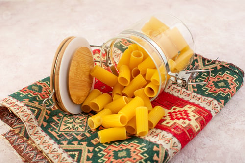 Preview: a front view raw italian pasta inside little glass kettle on the colorful carpet and light