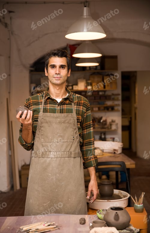 Preview: Handsome young man in pottery workshop holding clay