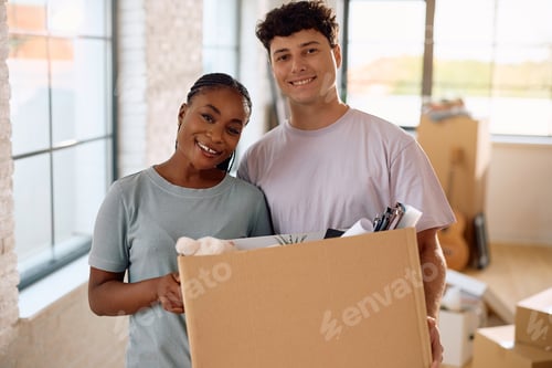 Preview: Happy multiracial couple relocating into new house and looking at camera.
