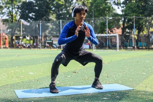 Preview: Full body of sporty male athlete do squates on mat at gym park