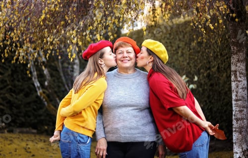 Preview: Granddaughter and daughter kissing their grandmother and mother in autumn garden