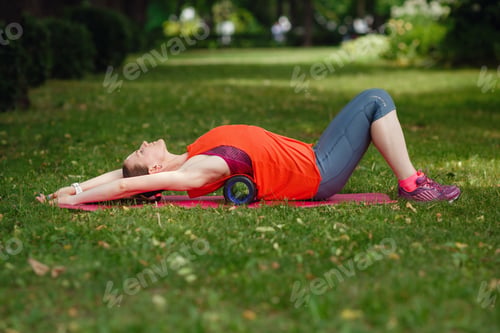Preview: A young woman does stretching with a special roller in the park.