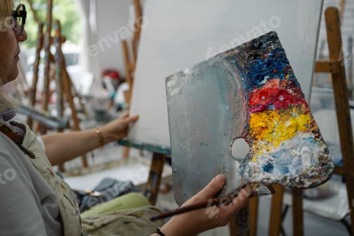 Preview: Senior woman artist holding palette and painting on canvas studio