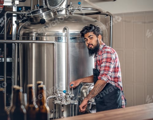 Preview: Indianr male manufacturer presenting craft beer in the microbrewery.